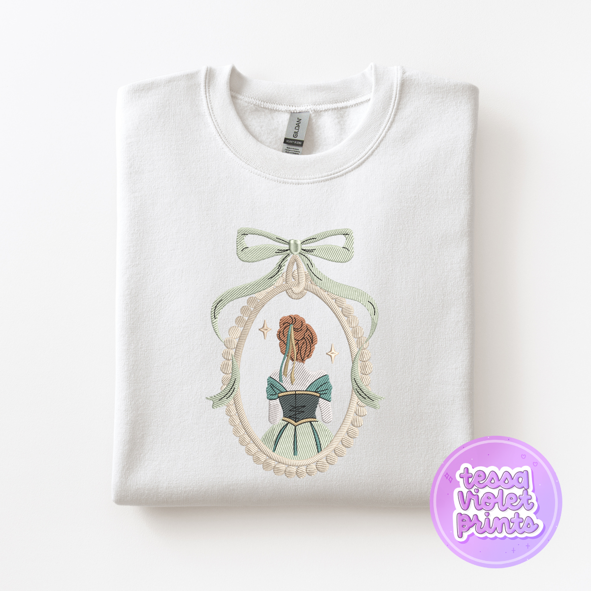 A white sweatshirt with a decorative embroidered design on the front, depicting a woman in a green dress with a bow.