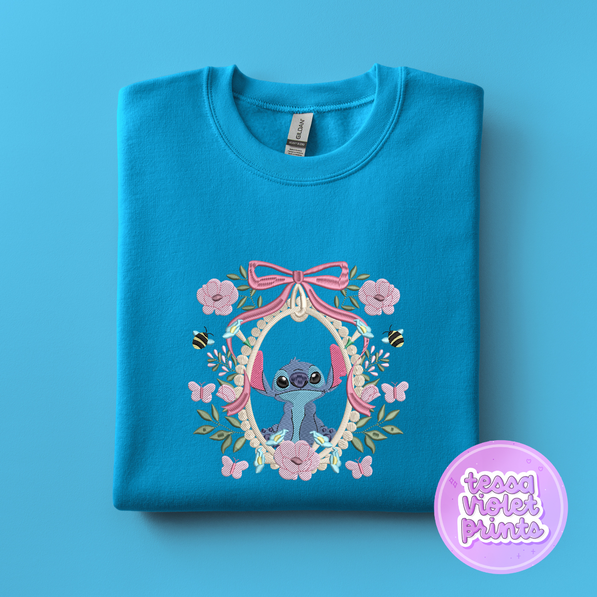 A blue t-shirt with a floral design and a small blue character, likely Stitch, inside an oval frame.
