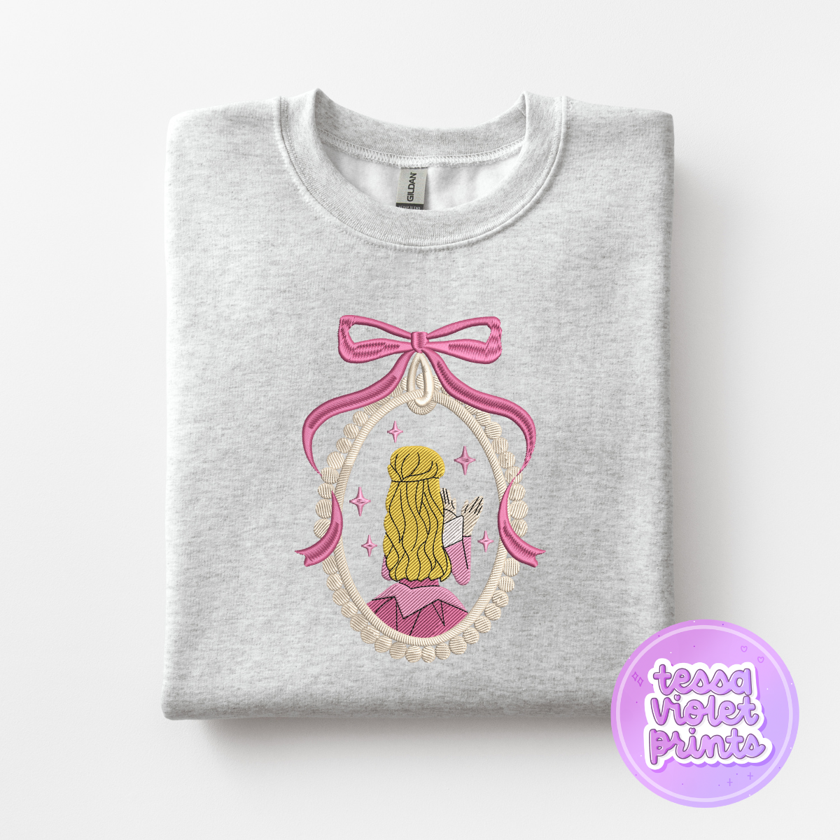 A gray sweatshirt with a pink bow and a framed illustration of a woman with blonde hair.
