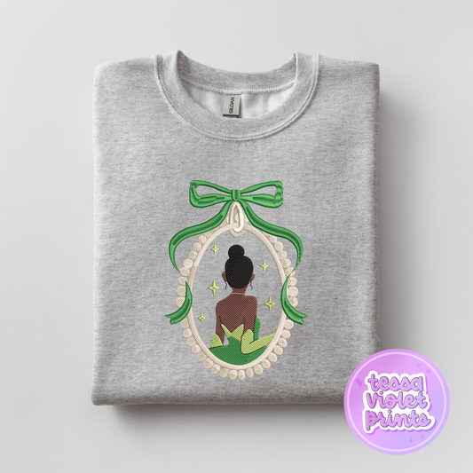 A gray sweatshirt with a green bow and a framed image of a woman with a green ribbon around her neck.