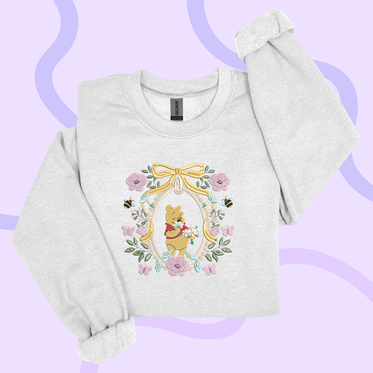 A gray sweatshirt with a floral design featuring a cartoon character, likely Winnie the Pooh, surrounded by flowers and leaves.