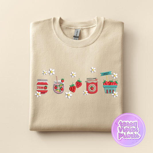A beige sweatshirt with a row of colorful jars and strawberries embroidered on it, along with white flowers.