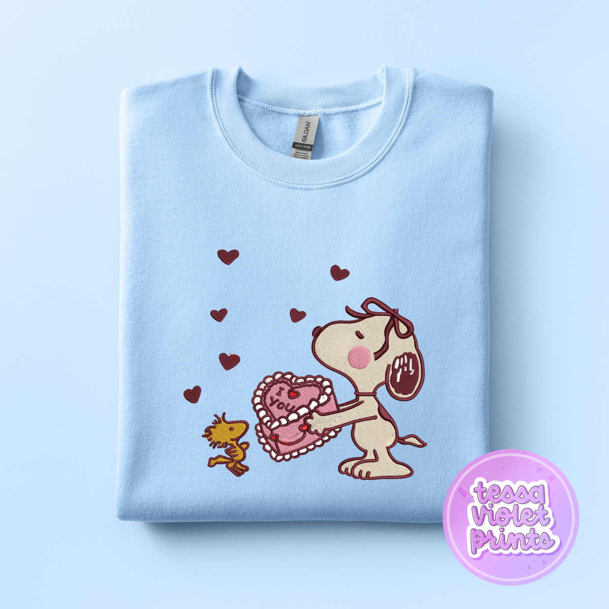 A light blue sweatshirt with a cartoon image of a dog holding a heart-shaped object and a smaller dog standing next to it, surrounded by hearts.