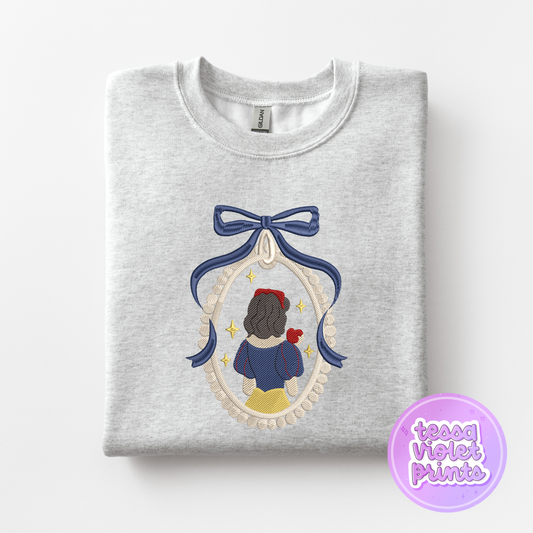 A gray sweatshirt with a blue ribbon and a framed image of a woman, likely representing the character Snow White from the Disney film.