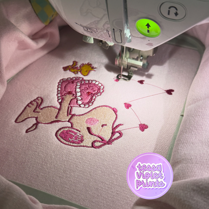 a pink fabric with a cartoon character, specifically a dog, and a heart-shaped design. The dog is lying down and appears to be smiling. The heart-shaped design is located above the dog, and there are several smaller hearts scattered around the dog.
