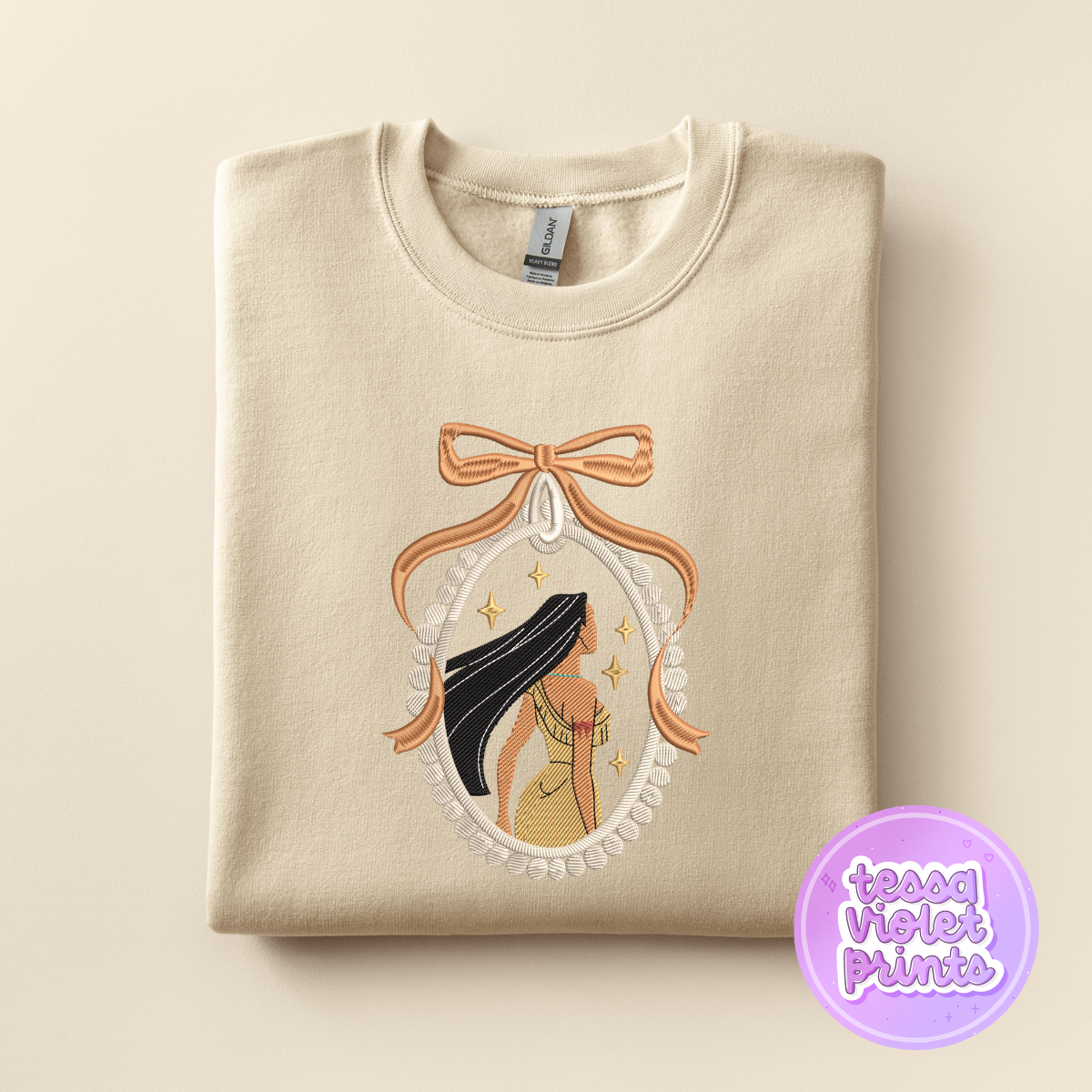 A beige sweatshirt with a decorative embroidered design featuring a woman with long hair and a bow.