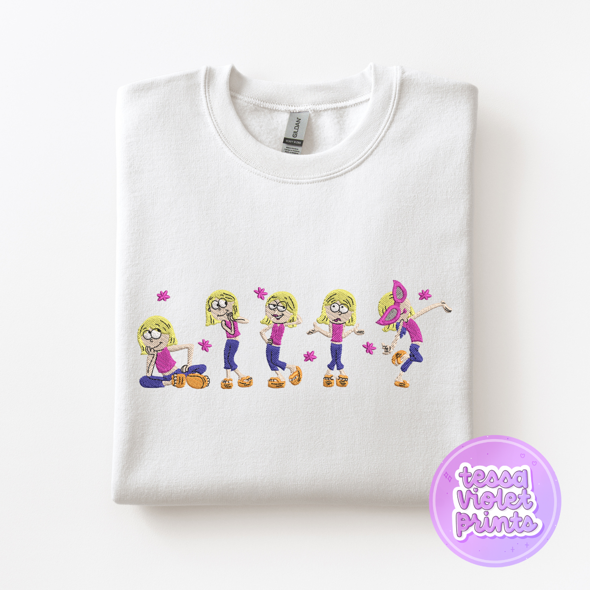 A white t-shirt with a line of five cartoon girl characters in various poses, including sitting, dancing, and jumping.