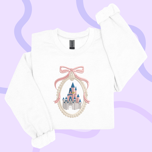 A white long-sleeved shirt with a pink bow and a castle embroidered on it, set against a purple background.