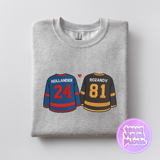 A gray sweatshirt with two hockey jerseys printed on it, featuring the names "Hollander" and "Rozanov" and the numbers "24" and "81" respectively.