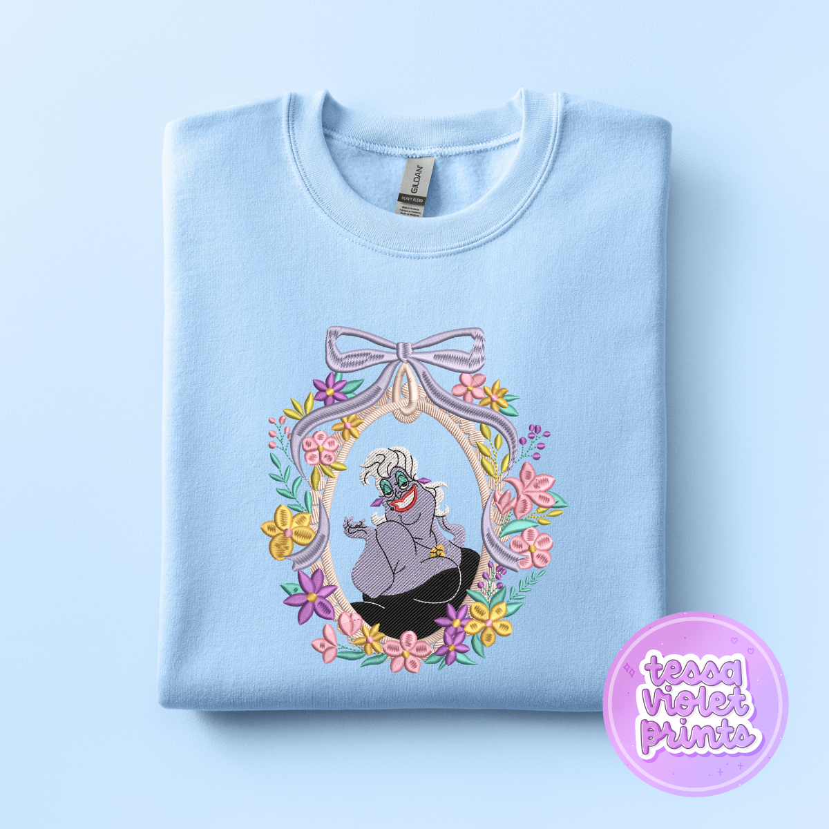 A light blue sweatshirt with a colorful floral wreath design featuring a character from the Disney animated film "The Little Mermaid".