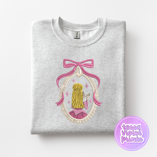 A gray sweatshirt with a pink bow and a framed illustration of a woman with blonde hair.