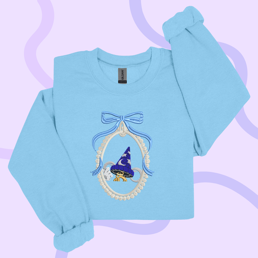 A light blue long-sleeved shirt with a blue bow and a wizard hat design on the front.