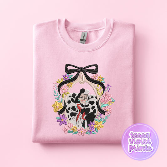A pink sweatshirt with a black bow and a floral wreath design featuring a Dalmatian character.