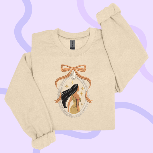 A beige sweater with an embroidered design featuring a woman's face and a bow.