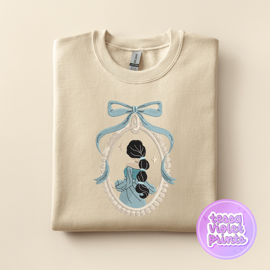 A beige sweater with a blue bow and a framed image of a woman with long hair, which appears to be a design or pattern.