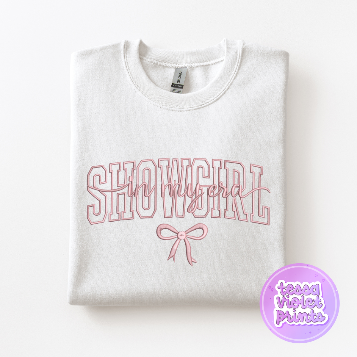 A white sweatshirt with the text "SHOWGIRL" printed on it, along with a pink bow.