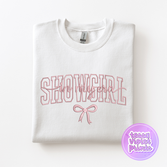 A white sweatshirt with the text "SHOWGIRL" printed on it, along with a pink bow.